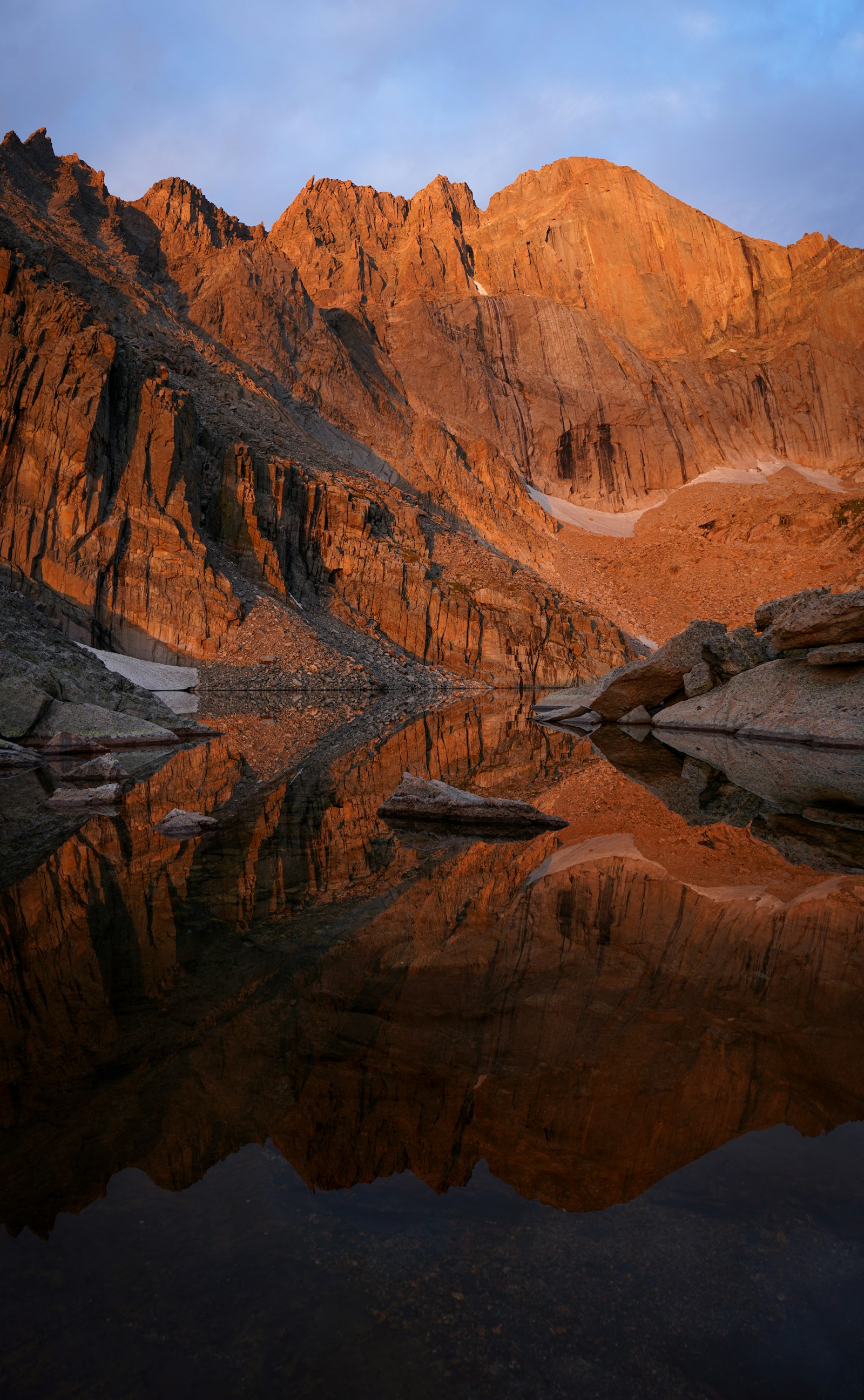 Mountain peaks reflected in a rocky alpine lake at sunrise.